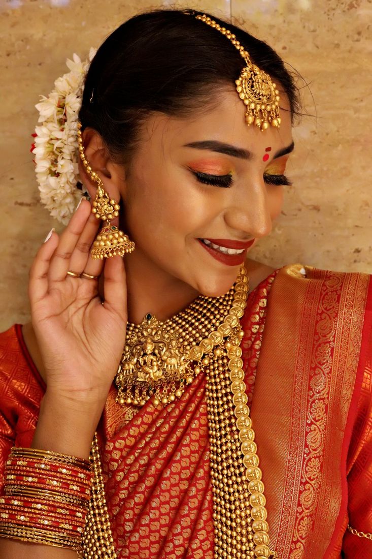 A bride wearing a gold temple necklace, jhumkas and maang tikka